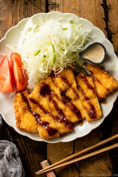 A white plate containing chicken katsu with tonkatsu sauce and shredded cabbage with sesame dressing.