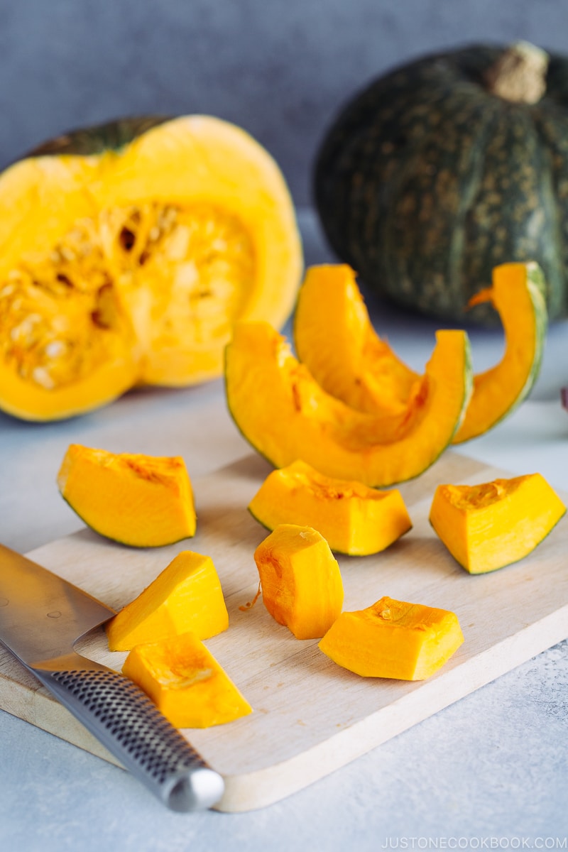 Kabocha being cut with a knife on a wooden cutting board.