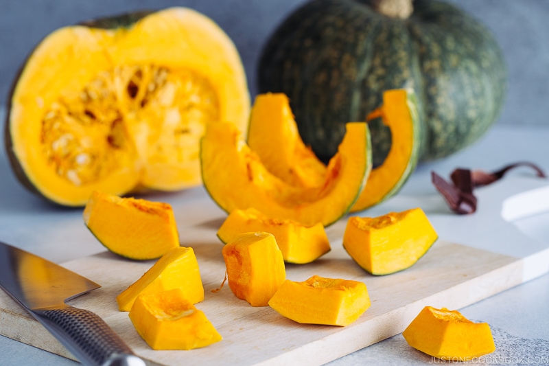 Kabocha being cut with a knife on a wooden cutting board.