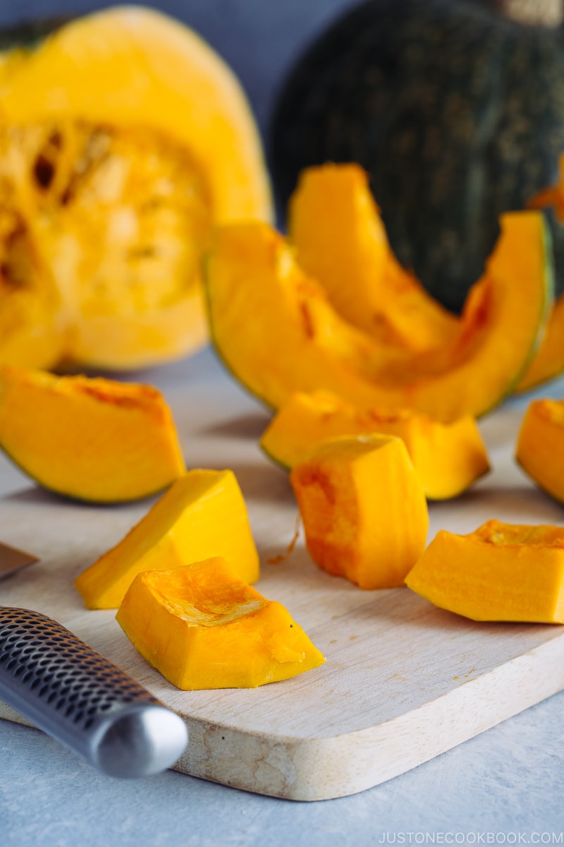 Kabocha being cut with a knife on a wooden cutting board.