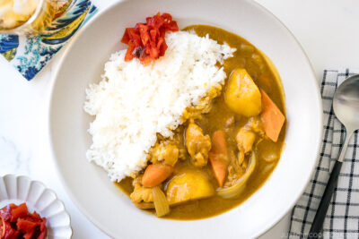 A ceramic bowl containing Japanese Chicken Curry along with steamed rice and fukujinzuke pickles.