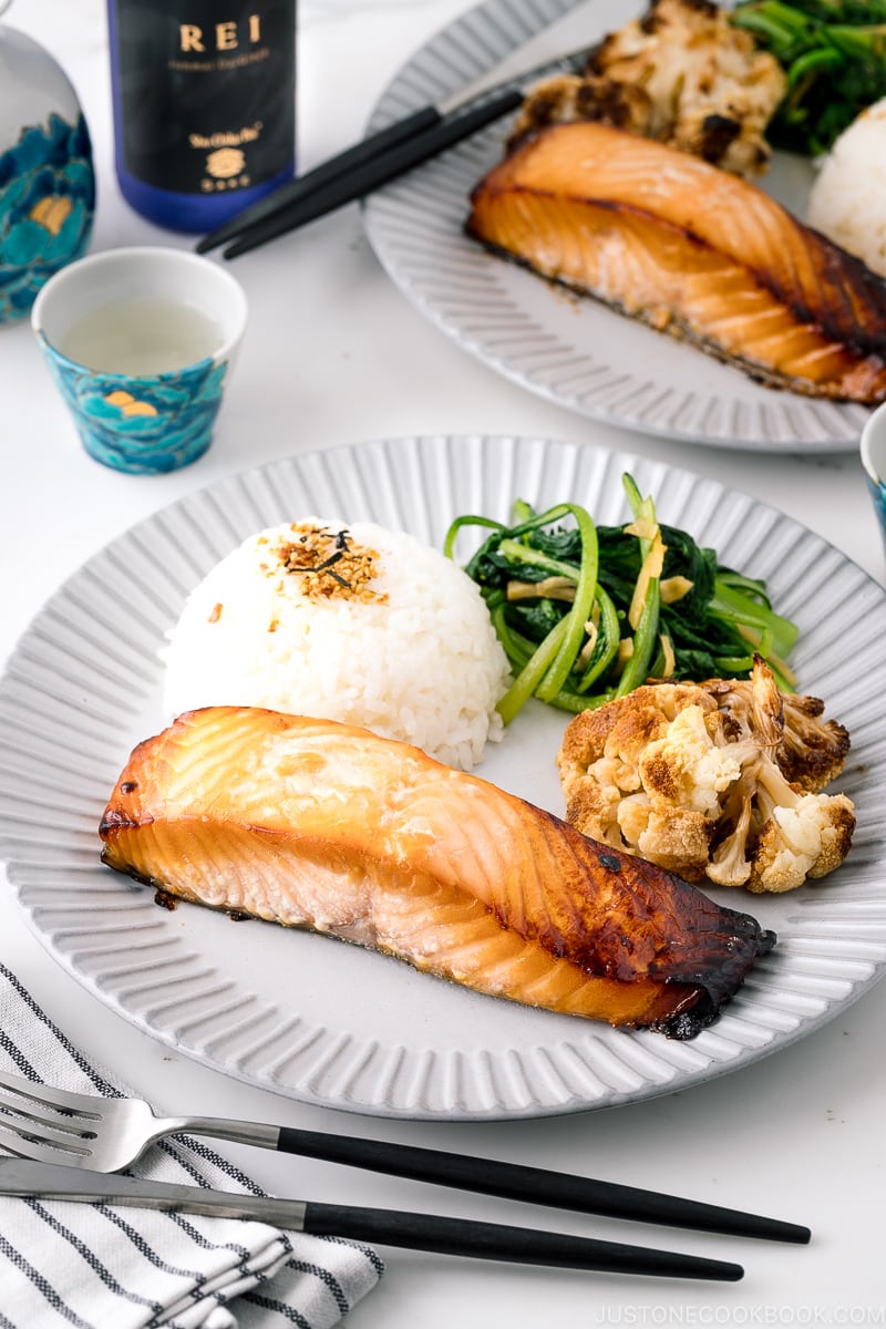 A ceramic plate containing Mirin Salmon along with steamed rice, roasted cauliflower, and sauteed greens.