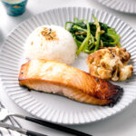 A ceramic plate containing Mirin Salmon along with steamed rice, roasted cauliflower, and sauteed greens.