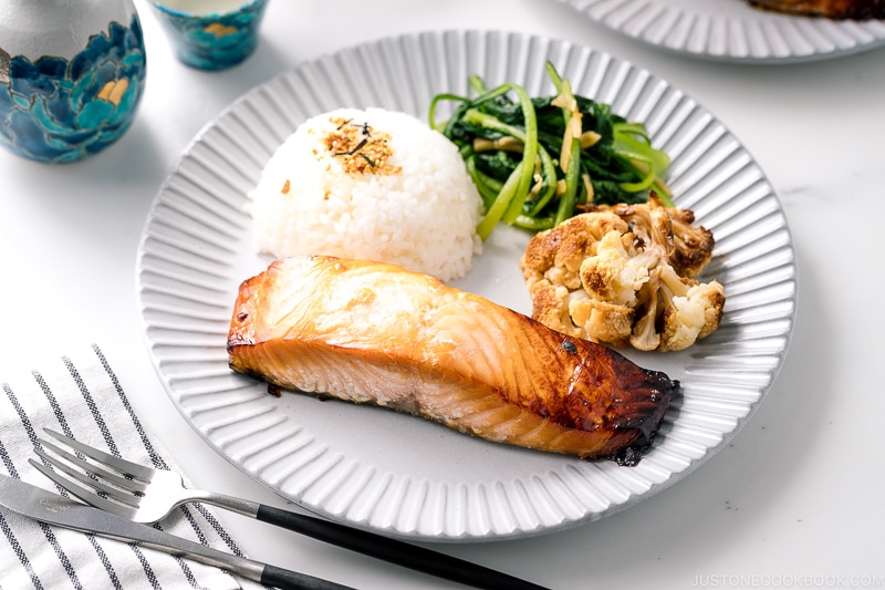 A ceramic plate containing Mirin Salmon along with steamed rice, roasted cauliflower, and sauteed greens.