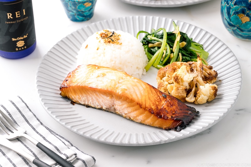 A ceramic plate containing Mirin Salmon along with steamed rice, roasted cauliflower, and sauteed greens.