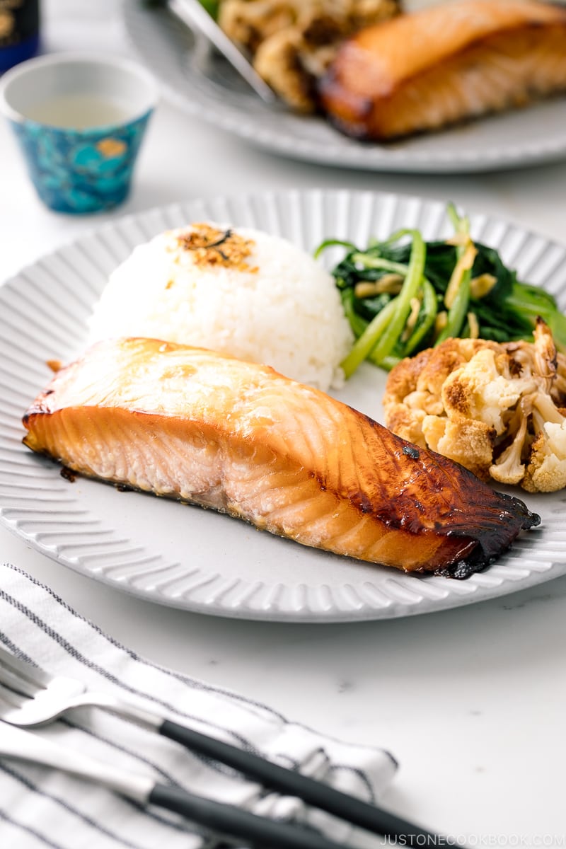 A ceramic plate containing Mirin Salmon along with steamed rice, roasted cauliflower, and sauteed greens.