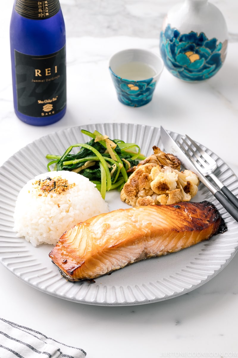 A ceramic plate containing Mirin Salmon along with steamed rice, roasted cauliflower, and sauteed greens.