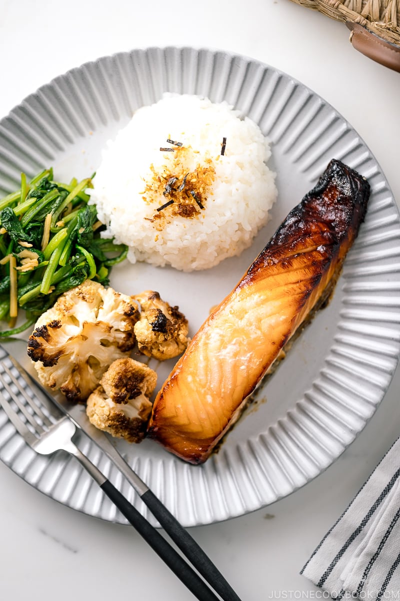 A ceramic plate containing Mirin Salmon along with steamed rice, roasted cauliflower, and sauteed greens.