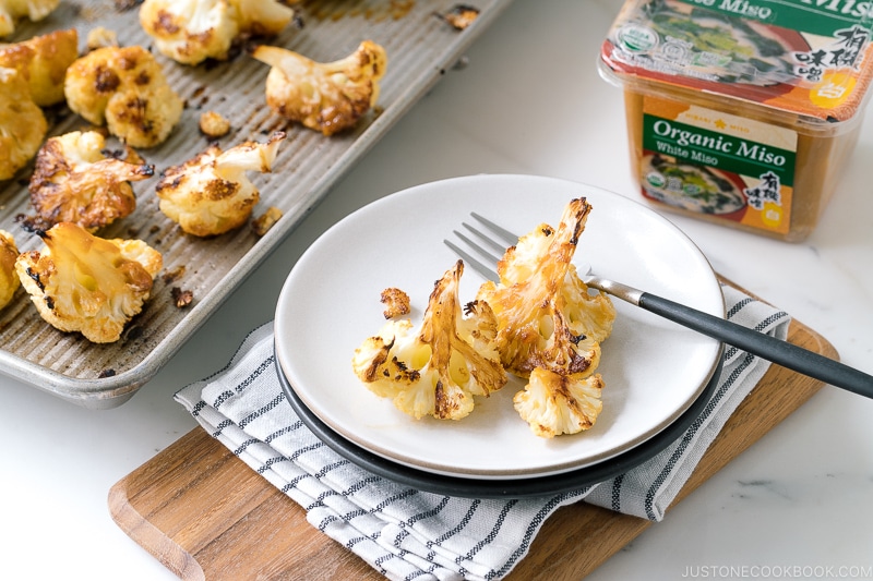 A baking sheet pan and a ceramic plate containing Roasted Miso Garlic Cauliflower.