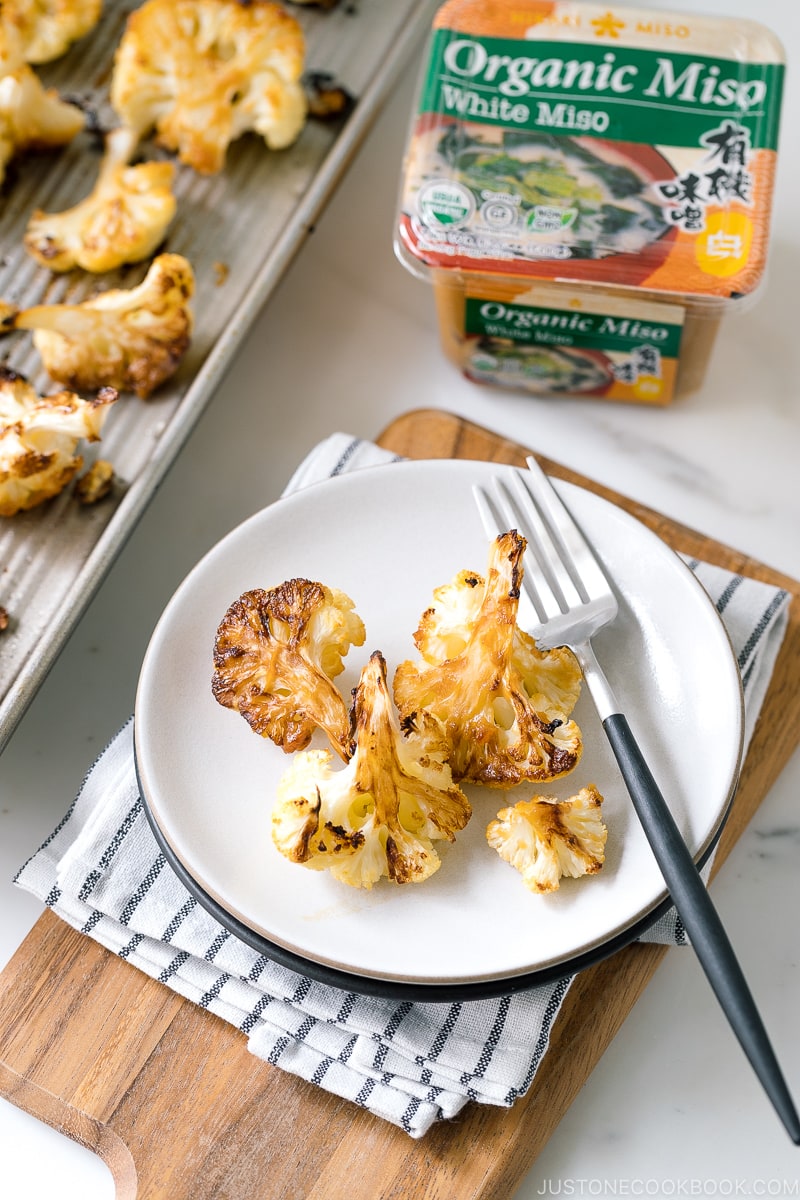 A baking sheet pan and a ceramic plate containing Roasted Miso Garlic Cauliflower.