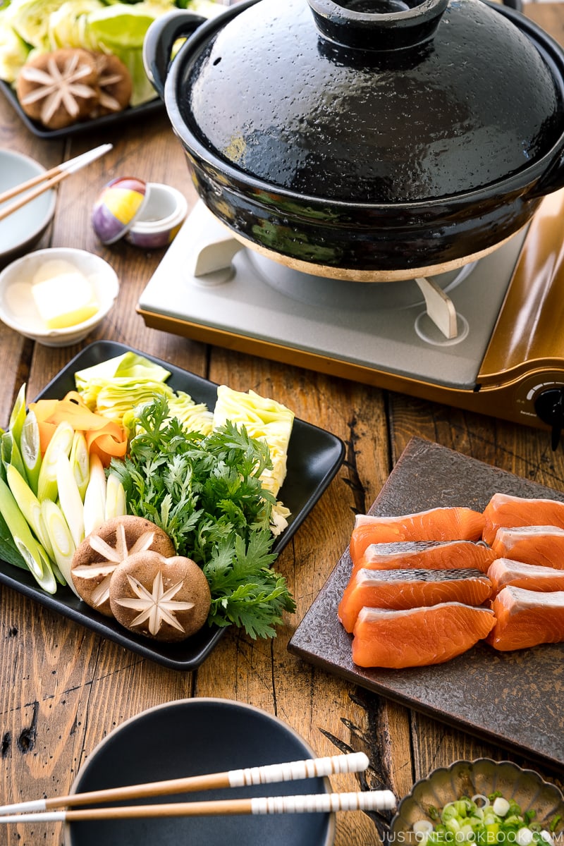 A Japanese donabe clay pot along with platters of vegetables and salmon.