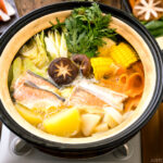 A Japanese donabe clay pot containing salmon, potato, daikon, corn, cabbage simmered in miso-based soup.