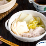 A donabe containing pork, cabbage, tofu, and mushrooms in a kombu broth.