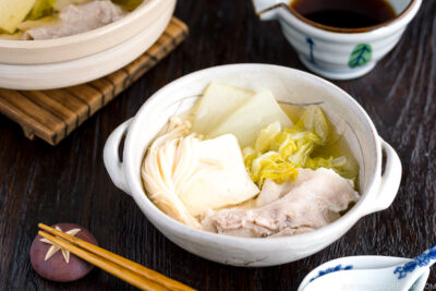 A donabe containing pork, cabbage, tofu, and mushrooms in a kombu broth.