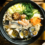 A donabe (earthenware hot pot) containing meat, seafood, and vegetables.