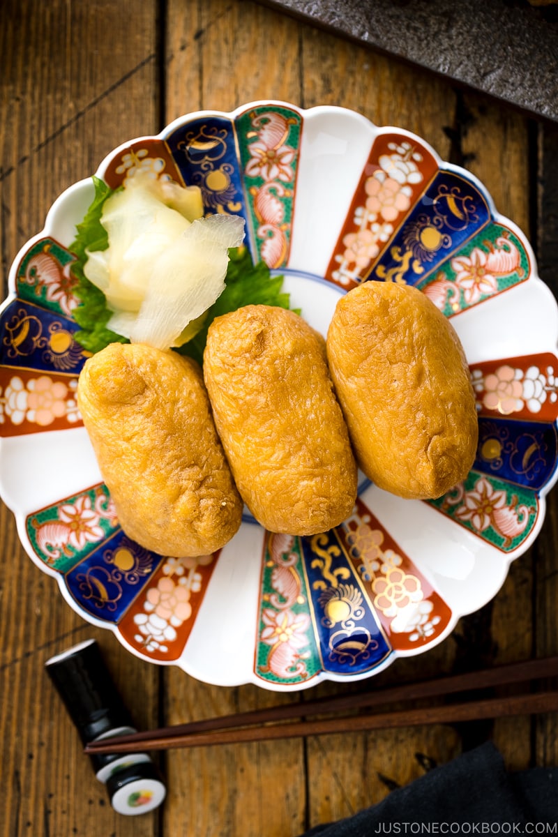 A Japanese plate containing inari sushi garnished with sushi ginger.