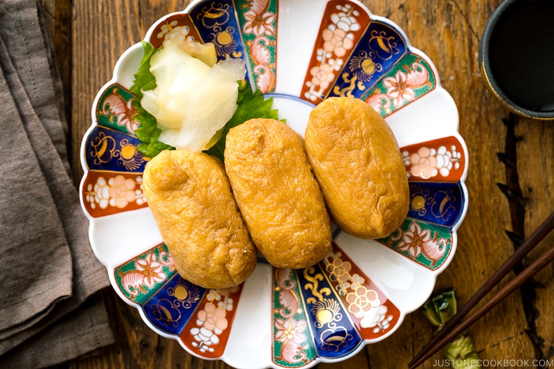 A Japanese plate containing inari sushi garnished with sushi ginger.