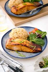 A blue and white plate containing miso salmon, ginger rice, and salad.