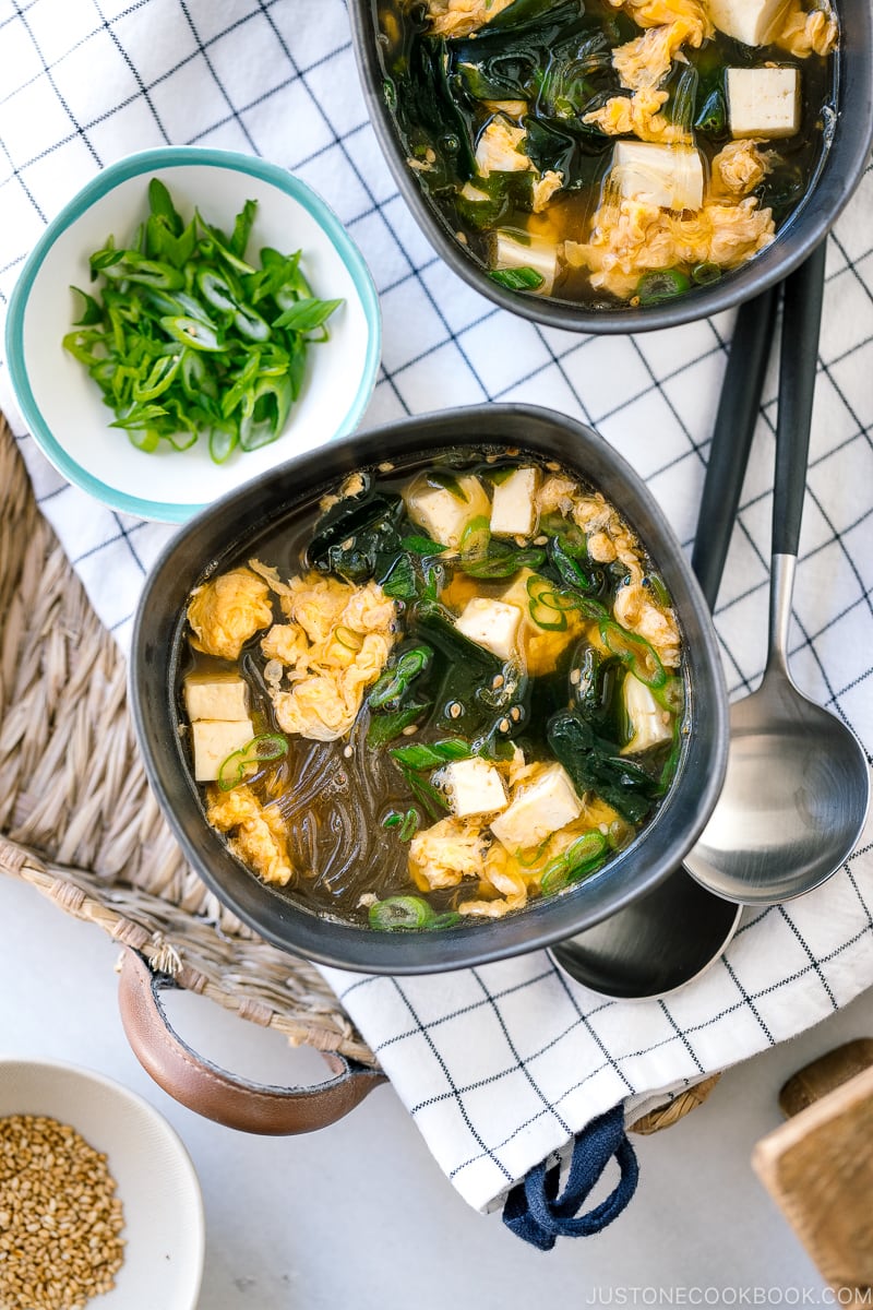 Black ceramic bowls containing glass noodle soup with tofu, fluffy egg, and wakame seaweed.