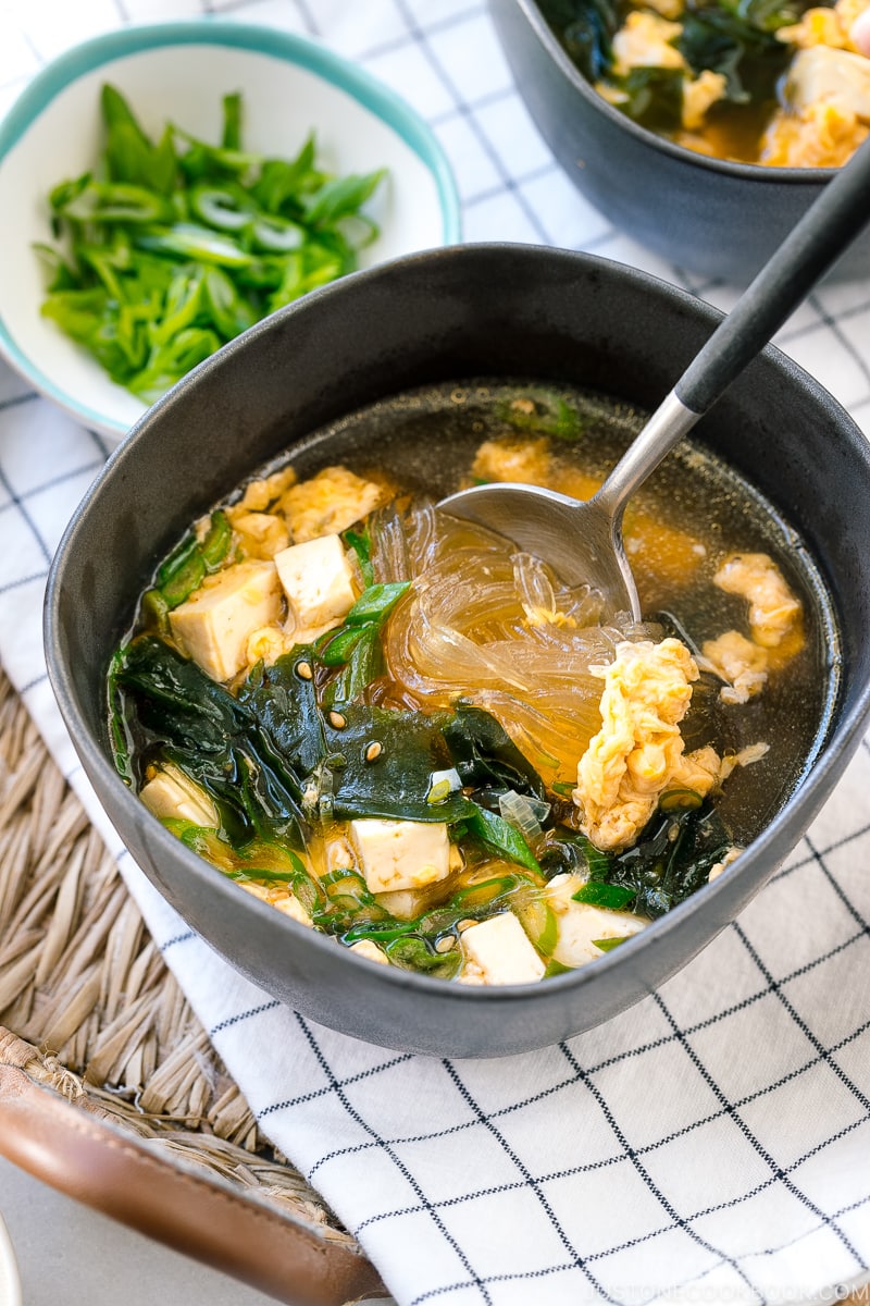 Black ceramic bowls containing glass noodle soup with tofu, fluffy egg, and wakame seaweed.