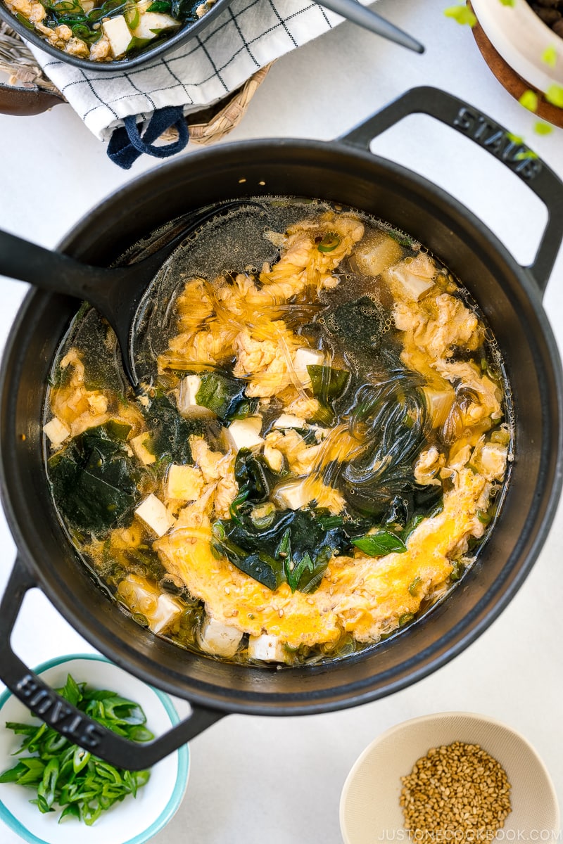 Black ceramic bowls containing glass noodle soup with tofu, fluffy egg, and wakame seaweed.