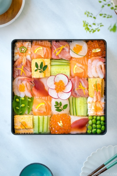 A Japanese lacquer box containing colorful Mosaic Sushi that's made of checkerboard pattern of various sashimi, tamago, and cucumber laid over sushi rice.