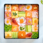 A Japanese lacquer box containing colorful Mosaic Sushi that's made of checkerboard pattern of various sashimi, tamago, and cucumber laid over sushi rice.