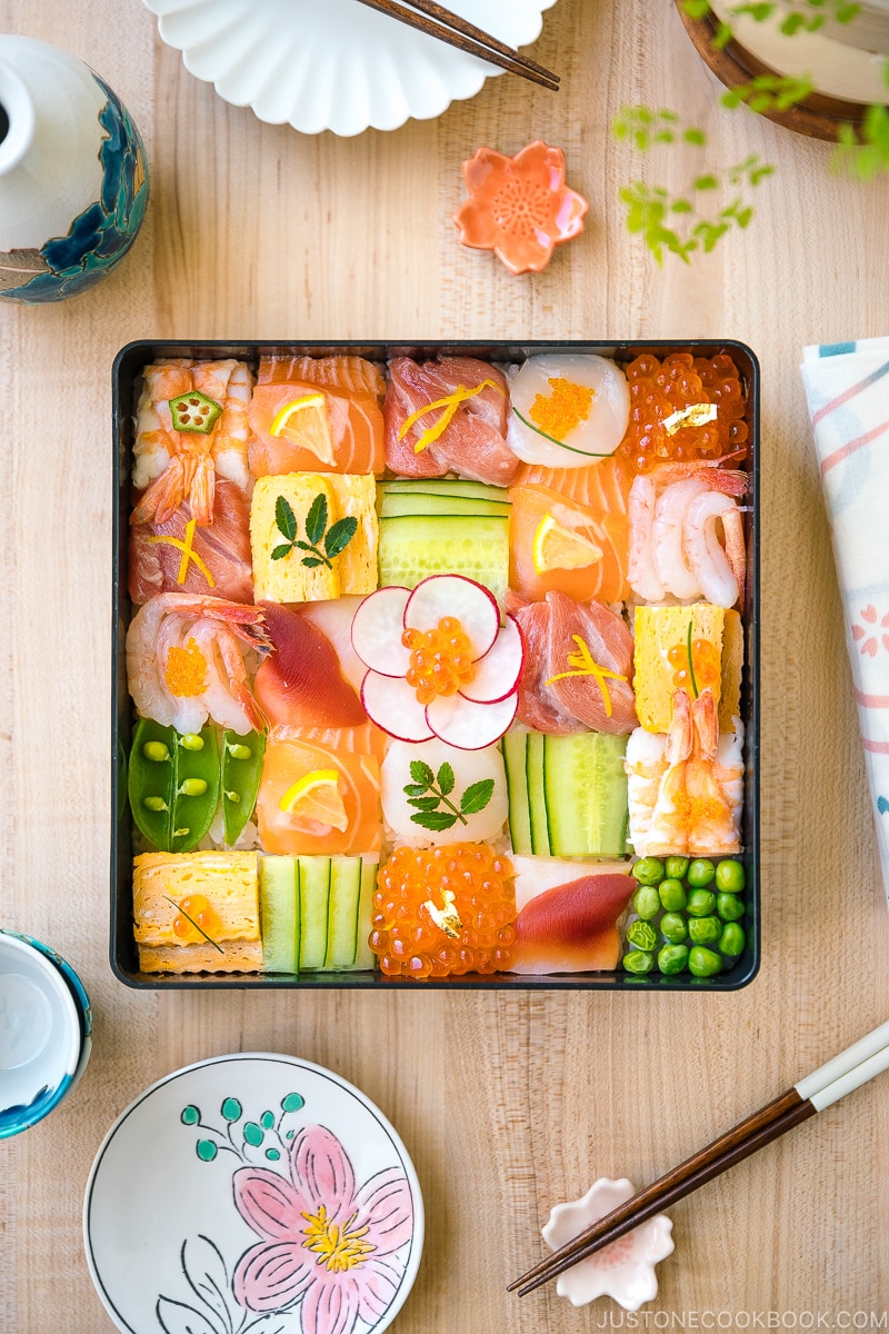 A Japanese lacquer box containing colorful Mosaic Sushi that's made of checkerboard pattern of various sashimi, tamago, and cucumber laid over sushi rice.