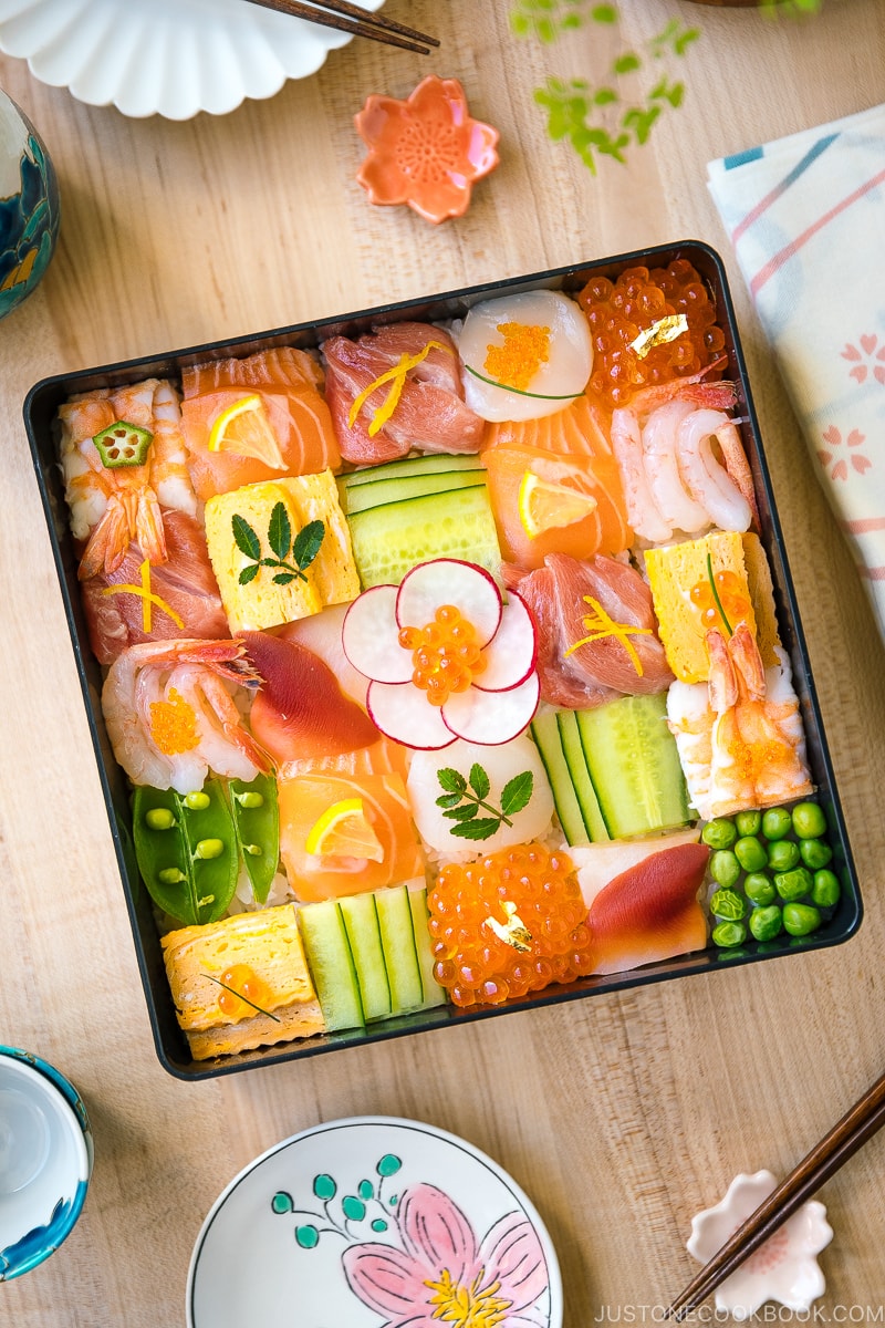 A Japanese lacquer box containing colorful Mosaic Sushi that's made of checkerboard pattern of various sashimi, tamago, and cucumber laid over sushi rice.