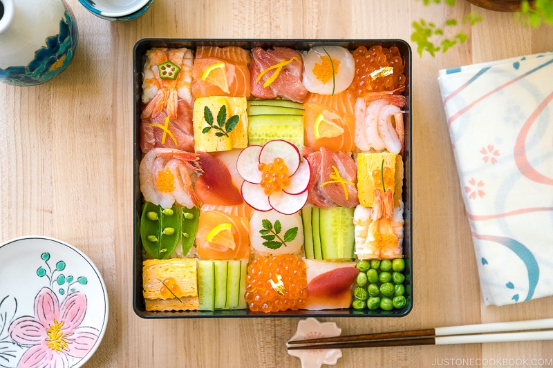 A Japanese lacquer box containing colorful Mosaic Sushi that's made of checkerboard pattern of various sashimi, tamago, and cucumber laid over sushi rice.