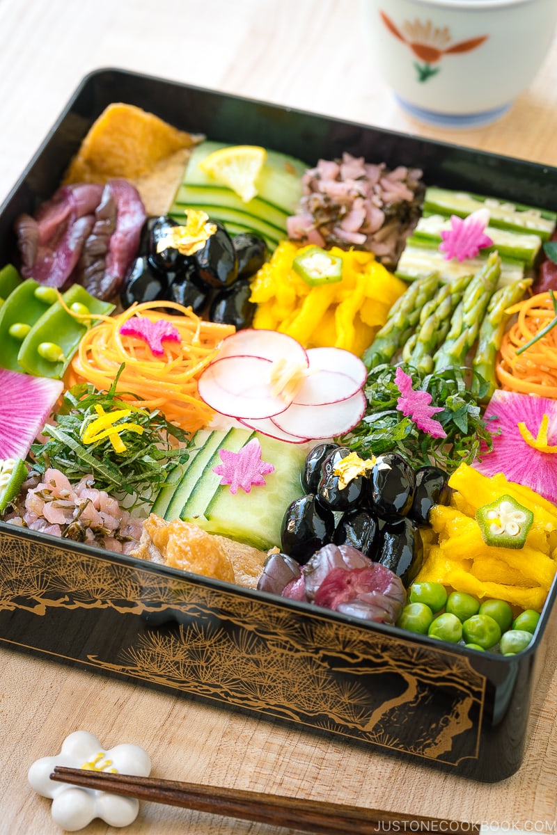 A Japanese lacquer box containing colorful Mosaic Sushi that's made of checkerboard pattern of various vegan-friendly ingredients laid over sushi rice.