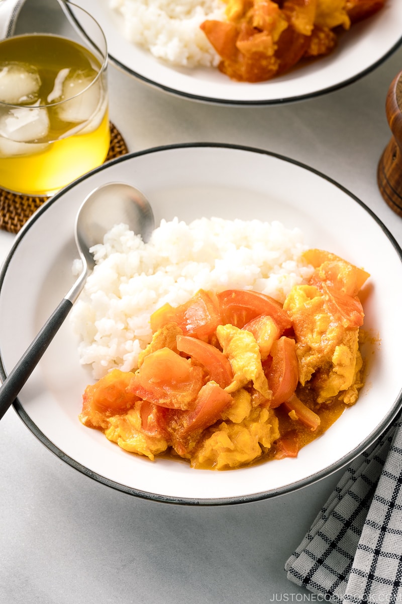 A white ceramic shallow bowl containing Stir-Fried Tomatoes and Eggs over steamed rice.