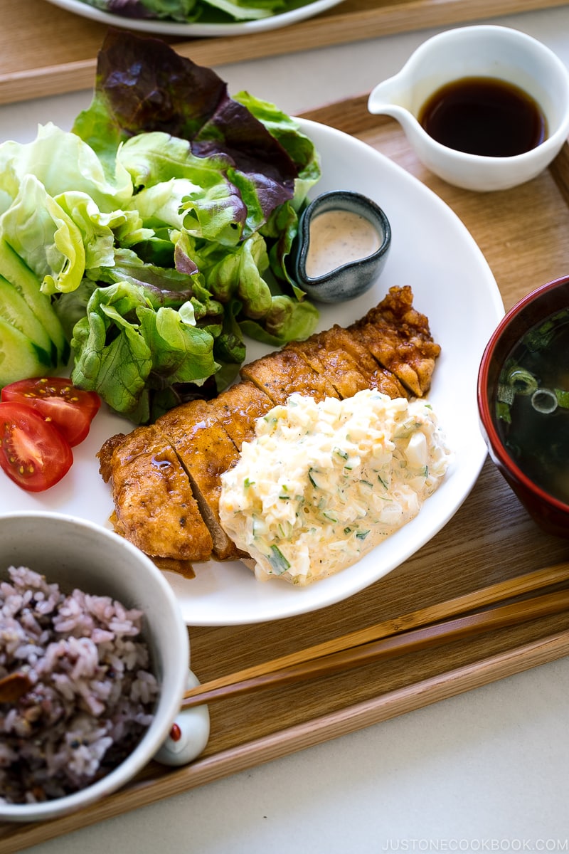 A white plate containing crispy chicken dressed with a tangy sauce and served with homemade tartar sauce.