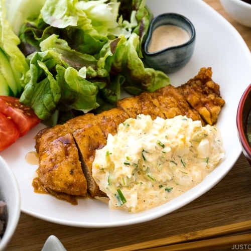 A white plate containing crispy chicken dressed with a tangy sauce and served with homemade tartar sauce.