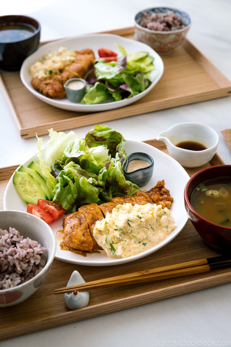 A white plate containing crispy chicken dressed with a tangy sauce and served with homemade tartar sauce.