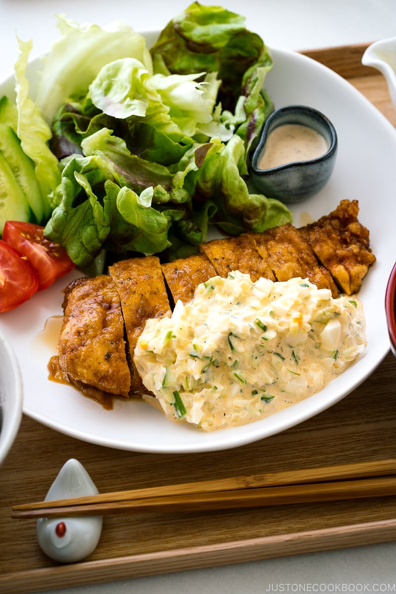 A white plate containing crispy chicken dressed with a tangy sauce and served with homemade tartar sauce.