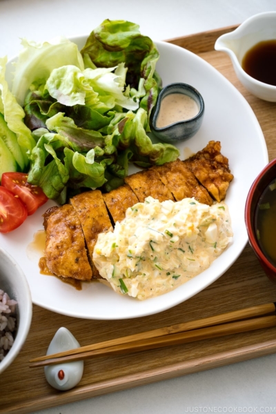 A white plate containing crispy chicken dressed with a tangy sauce and served with homemade tartar sauce.