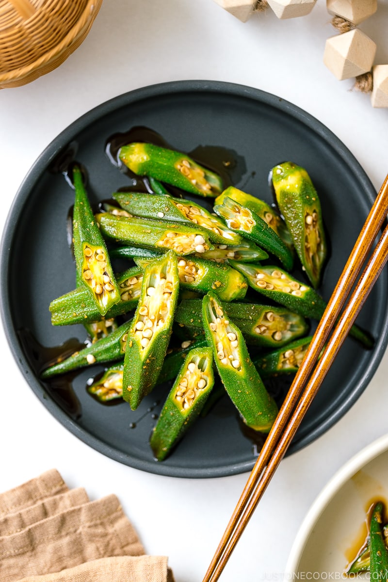 A black plate containing okra with ginger soy sauce.