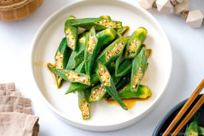 A white plate containing okra with ginger soy sauce.