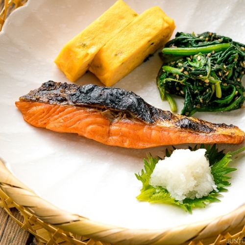 A white plate containing Japanese salted salmon (Shiozake), tamagoyaki, and spinach salad.