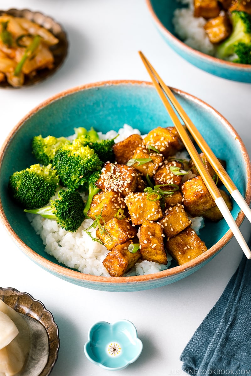 A taquoise bowl containing teriyaki tofu and broccoli over steamed rice.