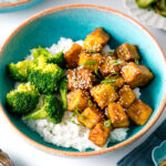 A taquoise bowl containing teriyaki tofu and broccoli over steamed rice.