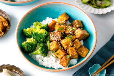 A taquoise bowl containing teriyaki tofu and broccoli over steamed rice.