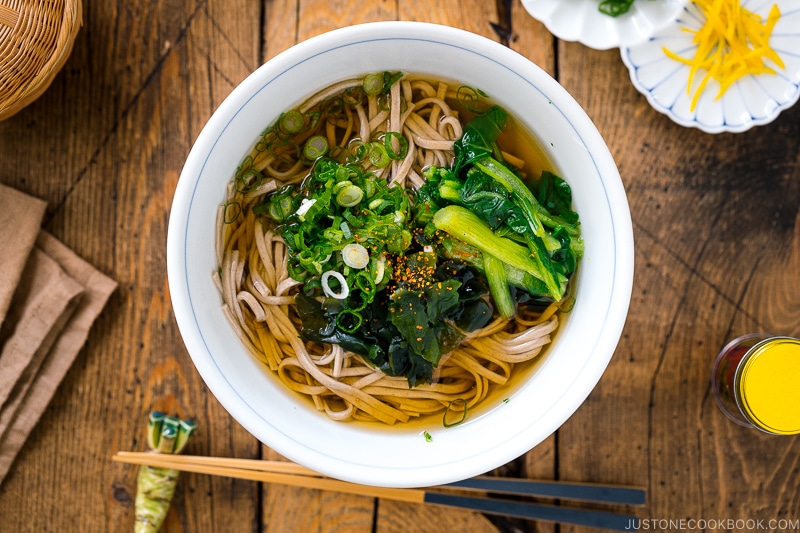 A bowl of simple soba noodle soup topped wakame seaweed, blanched komatsuna, and green onions.