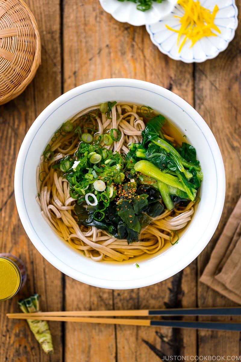 A bowl of simple soba noodle soup topped wakame seaweed, blanched komatsuna, and green onions.