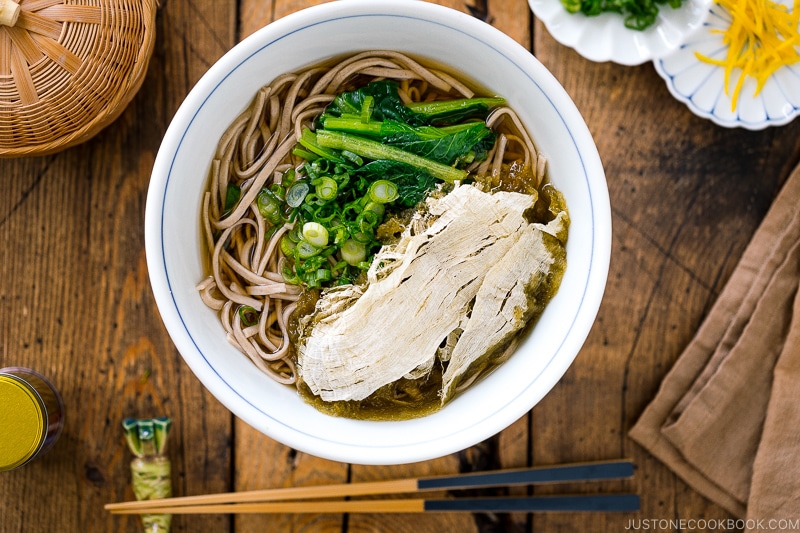A bowl of soba noodle soup topped with tororo kombu (a type of edible kelp), blanched komatsuna, and green onions.