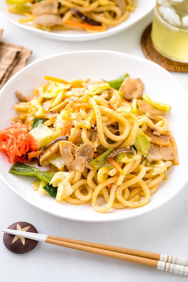 A white round plate containing Yaki Udon (Japanese Stir-Fried Udon Noodles) garnished with red pickled ginger.