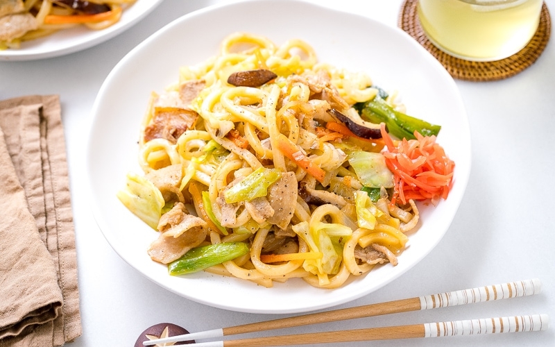 A white round plate containing Yaki Udon (Japanese Stir-Fried Udon Noodles) garnished with red pickled ginger.