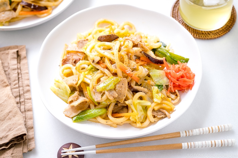 A white round plate containing Yaki Udon (Japanese Stir-Fried Udon Noodles) garnished with red pickled ginger.