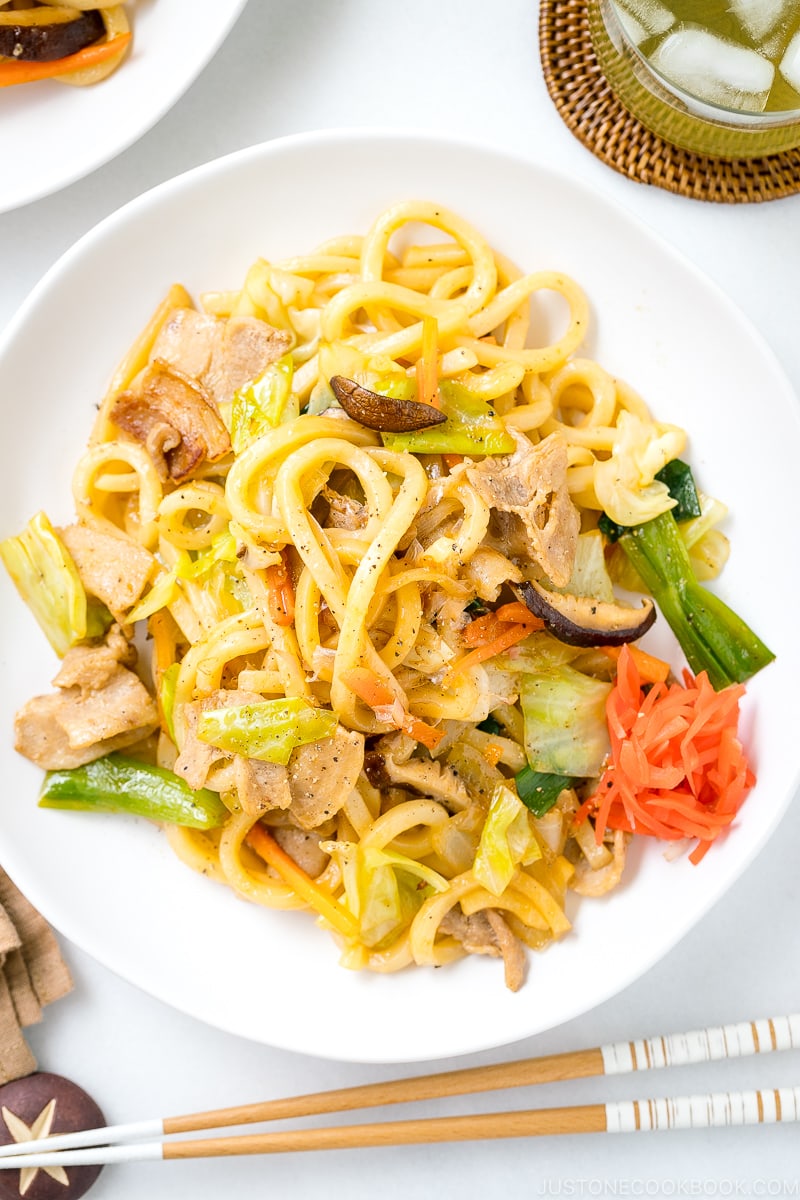 A white round plate containing Yaki Udon (Japanese Stir-Fried Udon Noodles) garnished with red pickled ginger.